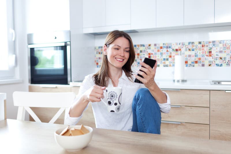 Junge Frau, die Handy in der Küche verwendet lizenzfreie stockbilder