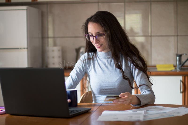 Junge Frau, die Rechnungen mit Debitkarte von zu Hause bezahlt stockfotografie