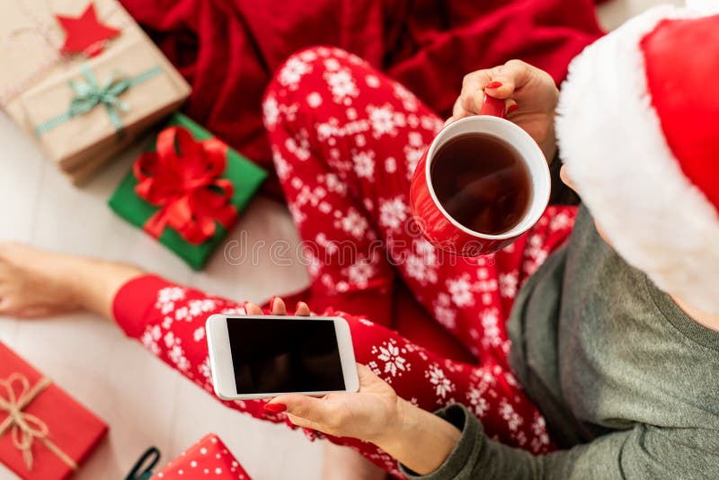 Junge Frau, die Sankt-Hut und Weihnachtspyjamas sitzen auf dem Boden unter den eingewickelten Weihnachtsgeschenken, kaufend an ih stockbild Junge Frau, die Sankt-Hut und Weihnachtspyjamas sitzen auf dem Boden unter den eingewickelten Weihnachtsgeschenken, kaufend an ih stockbild