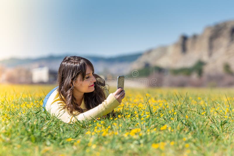 Junge Frau, die unter Verwendung des Handys niederlegt lizenzfreies stockfoto Junge Frau, die unter Verwendung des Handys niederlegt lizenzfreies stockfoto