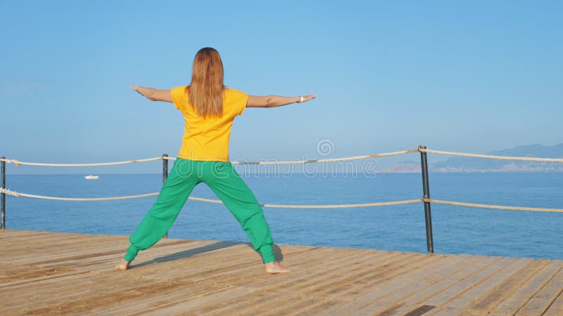 Junge Frau, die die Verlängerung am Holz Pier vor dem Hintergrund des Meeres oder des Ozeans macht.