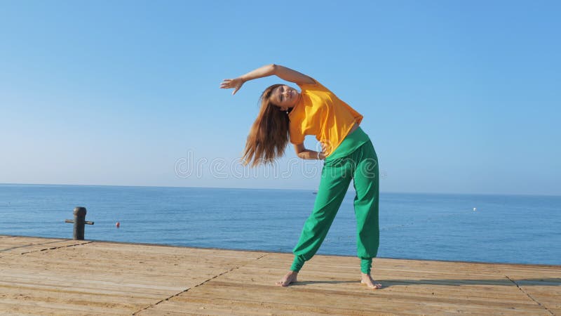 Junge Frau, die die Verlängerung am Holz Pier vor dem Hintergrund des Meeres oder des Ozeans macht.