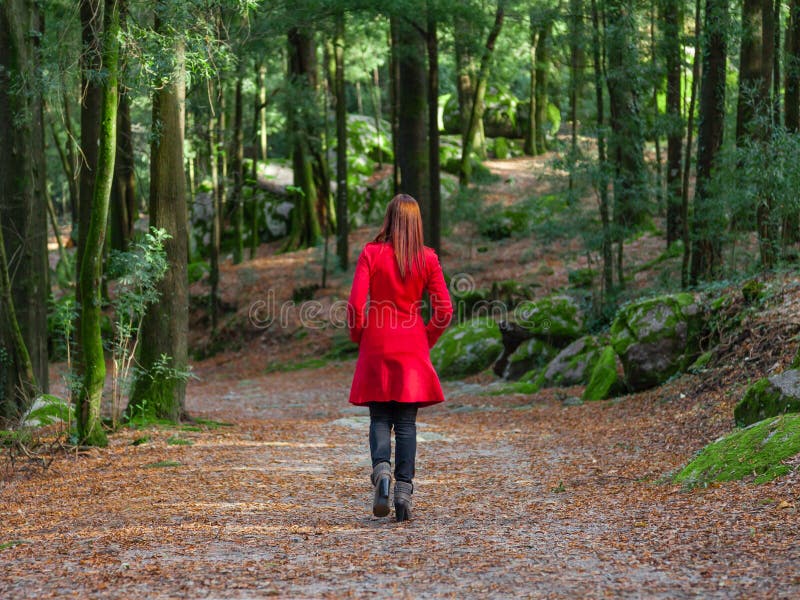 Junge Frau, die weg allein auf den Waldweg trägt roten langen Mantel geht