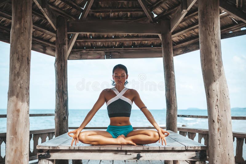 Junge Frau, die Yoga im hölzernen Gazebo am Strand macht stockbilder Junge Frau, die Yoga im hölzernen Gazebo am Strand macht stockbilder