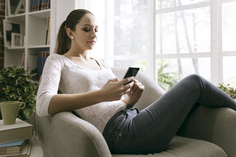 Junge Frau, die zu Hause an ihren Smartphone anschließt lizenzfreie stockfotos Junge Frau, die zu Hause an ihren Smartphone anschließt lizenzfreie stockfotos