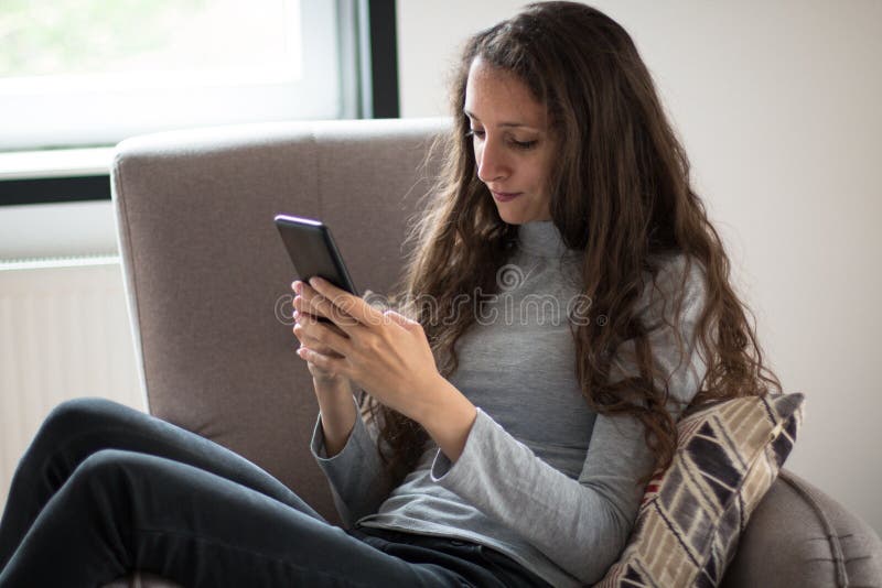 Junge Frau entspannt sich zu Hause auf ihrem Stuhl mit Smartphone stockbilder