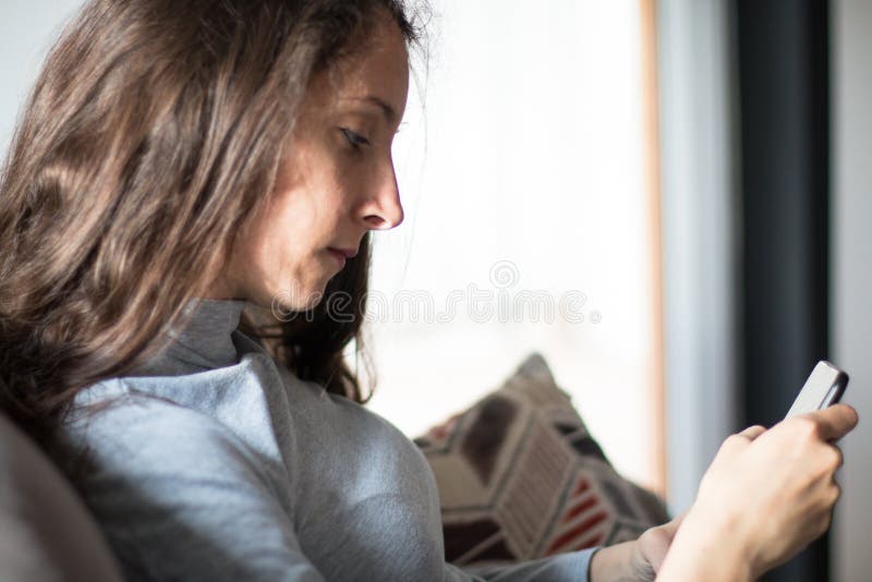 Junge Frau entspannt sich zu Hause auf ihrem Stuhl mit Smartphone lizenzfreie stockbilder
