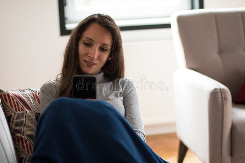 Junge Frau entspannt sich zu Hause mit Smartphone lizenzfreies stockfoto