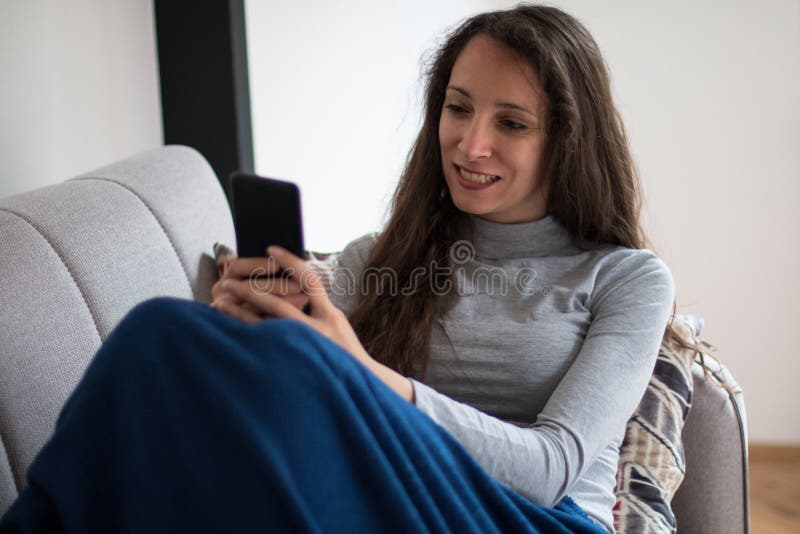Junge Frau entspannt sich zu Hause mit Smartphone lizenzfreies stockbild