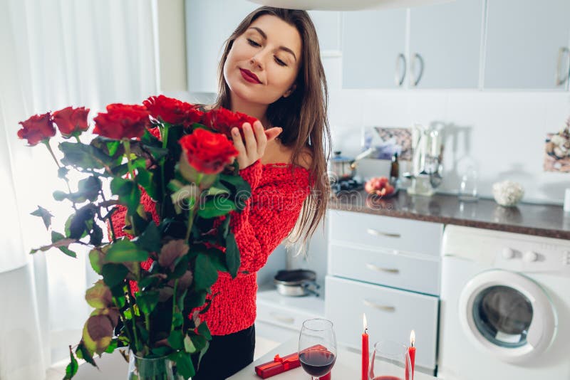 Junge Frau fand rote Rosen mit Kerze, Wein und Geschenkbox auf Küche Riechende Blumen des glücklichen Mädchens Rote Rose stockfotografie Junge Frau fand rote Rosen mit Kerze, Wein und Geschenkbox auf Küche Riechende Blumen des glücklichen Mädchens Rote Rose stockfotografie