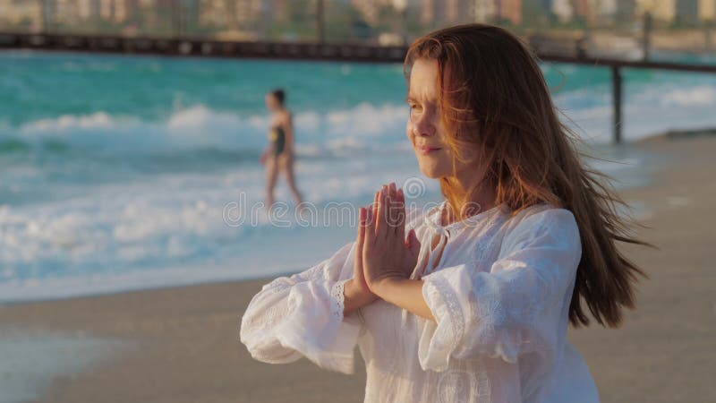 Junge Frau hält Armpalmen im namaste am sandigen Strand zusammen.