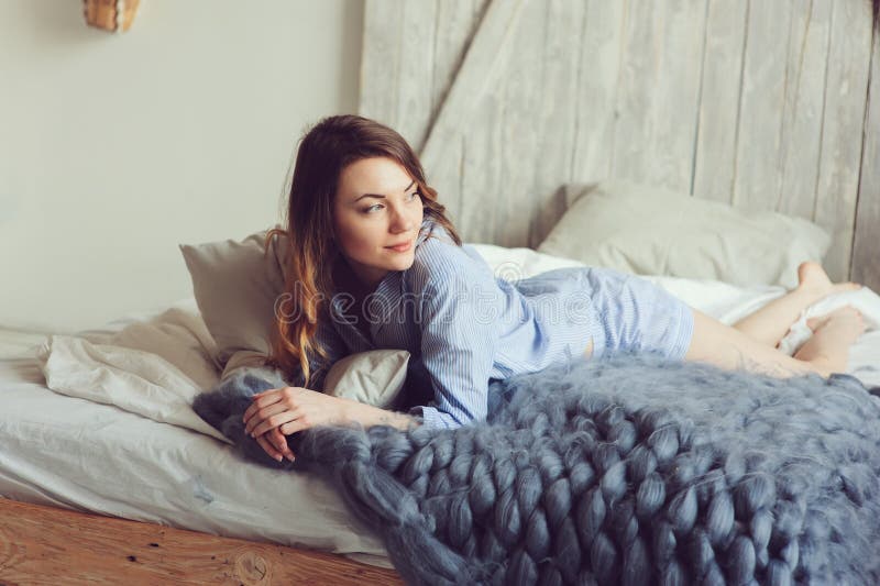 Junge Frau im Pyjama wachen morgens im gemütlichen skandinavischen Schlafzimmer und im Lügen auf Bett mit gestrickter Überformatd stockbild Junge Frau im Pyjama wachen morgens im gemütlichen skandinavischen Schlafzimmer und im Lügen auf Bett mit gestrickter Überformatd stockbild