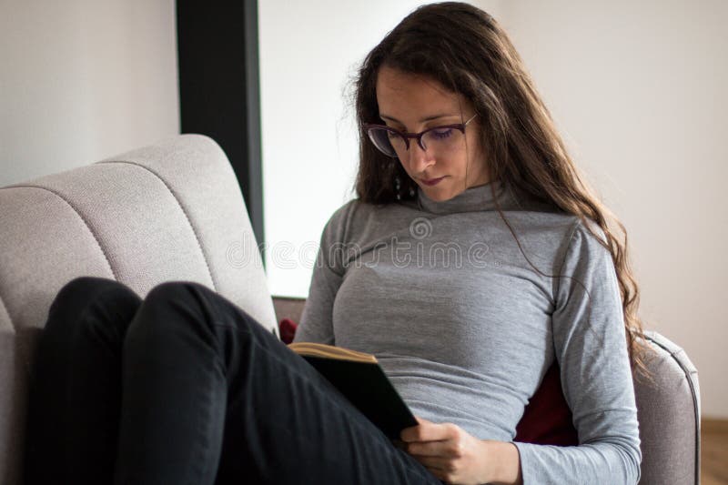 Junge Frau las drinnen ein gedrucktes Buch auf ihrem Sofa lizenzfreie stockbilder