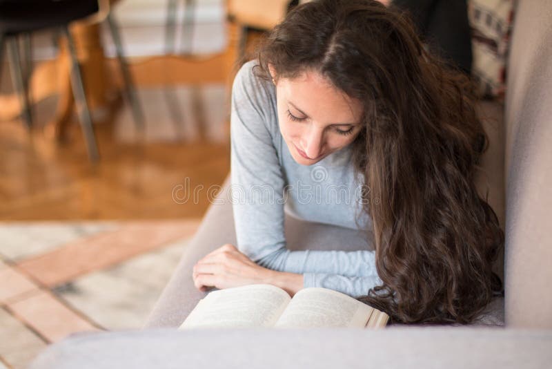 Junge Frau liegt auf dem Sofa und liest ein interessantes Buch stockbild