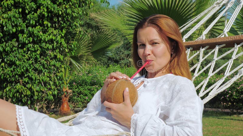 Junge Frau liegt in einer Hängematte mit Kokosnusswassercocktail.