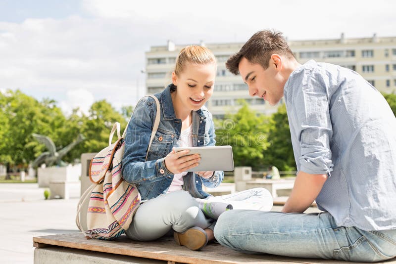 Junge Frau mit dem männlichen Freund, der digitale Tablette am Collegecampus verwendet lizenzfreies stockfoto Junge Frau mit dem männlichen Freund, der digitale Tablette am Collegecampus verwendet lizenzfreies stockfoto