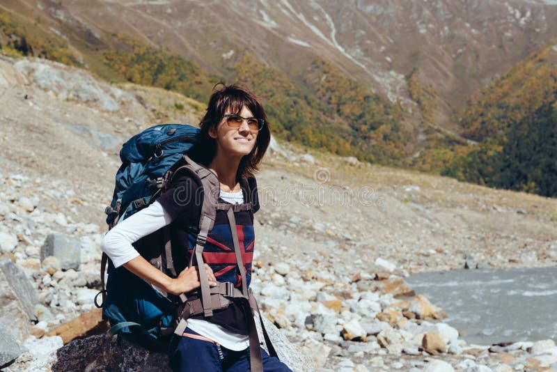 Junge Frau mit einem Rucksack in den Bergen sitzt auf einem Stein, der den Blick auf die Berge beruht und stockfotografie