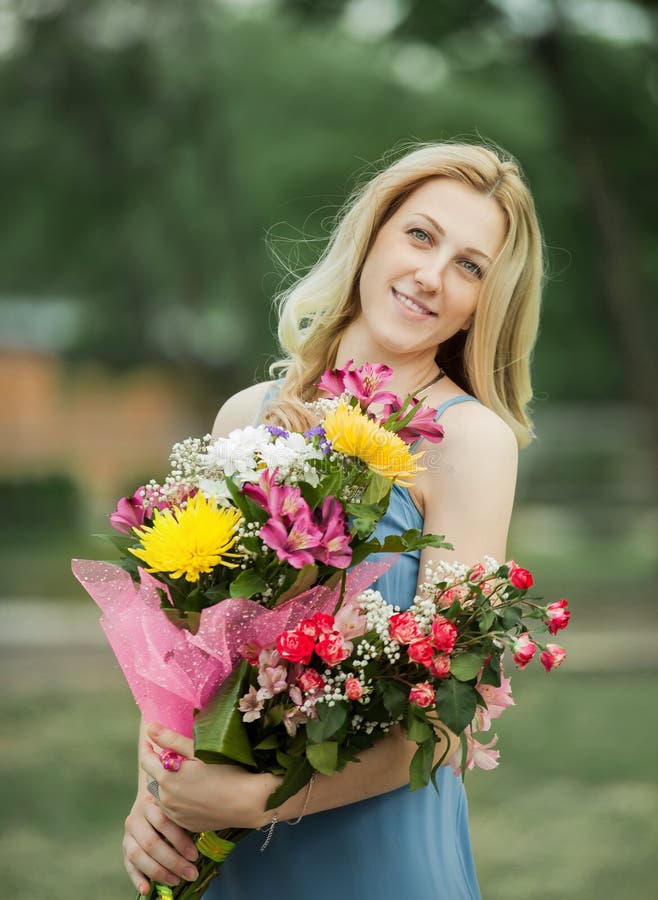 Junge Frau mit einem Strauß von Blumen auf einem unscharfen Hintergrund der Natur stockbild