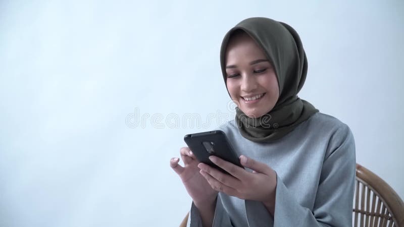 Junge Frau schreibt eine Botschaft auf ihrem Handy. Hijab Frau, die auf einem Stuhl sitzen und ein Handy hält