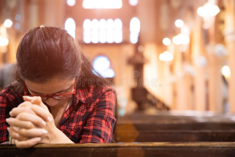 Junge Frau sitzt auf einer Bank in der Kirche und betet zum Gott Hände gefaltet im Gebetskonzept für Glauben