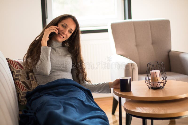 Junge Frau telefoniert und trinkt Kaffee im Wohnzimmer stockfoto
