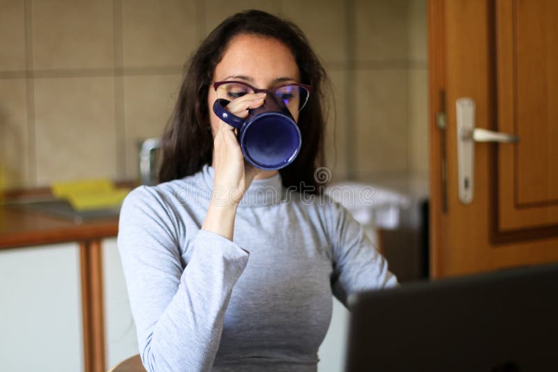 Junge Frau trinkt Kaffee in ihrem Wohnzimmer, während sie am Computer arbeitet lizenzfreie stockfotografie