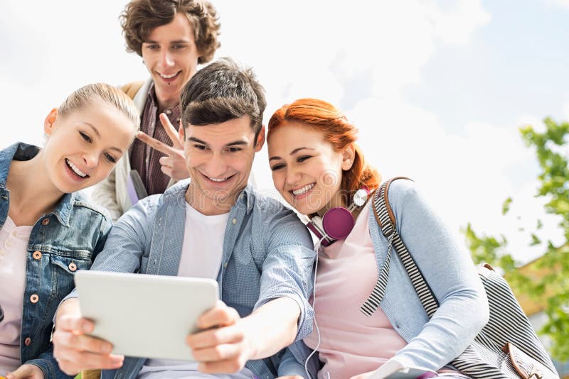 Junge Freunde, die durch digitale Tablette am Collegecampus sich fotografieren stockbild Junge Freunde, die durch digitale Tablette am Collegecampus sich fotografieren stockbild