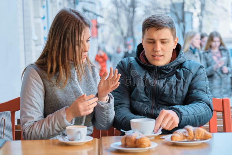 Junge Freunde Mann und Frau, die in des im Freien trinkendem Teekaffee Cafés mit Hörnchen sprechen lizenzfreie stockfotos Junge Freunde Mann und Frau, die in des im Freien trinkendem Teekaffee Cafés mit Hörnchen sprechen lizenzfreie stockfotos