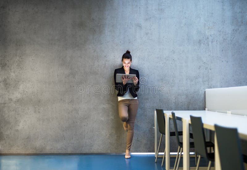 Junge Geschäftsfrau mit Tablettenstellung gegen Betonmauer im Büro lizenzfreie stockbilder Junge Geschäftsfrau mit Tablettenstellung gegen Betonmauer im Büro lizenzfreie stockbilder