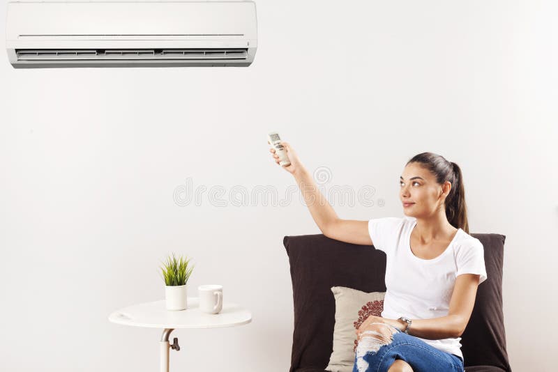 Junge gl?ckliche Frau, die zu Hause auf Couch-funktionierender Klimaanlage mit Fernbedienung sitzt stockfotos Junge gl?ckliche Frau, die zu Hause auf Couch-funktionierender Klimaanlage mit Fernbedienung sitzt stockfotos