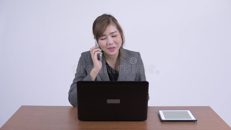 Junge glückliche asiatische Geschäftsfrau, die am Telefon bei der Arbeit spricht