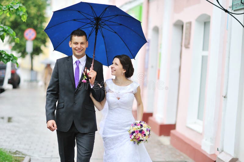 Junge glückliche Hochzeitspaare, die durch den Regen in einer alten Stadt gehen stockbild Junge glückliche Hochzeitspaare, die durch den Regen in einer alten Stadt gehen stockbild