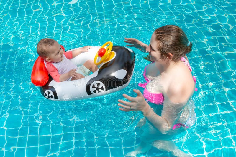 Junge glückliche Mutter in einem rosa Bikini, der Spaß und Fangbaby im Pool hat Ein frohes kleines Kind sitzt in einem aufblasbar lizenzfreie stockbilder Junge glückliche Mutter in einem rosa Bikini, der Spaß und Fangbaby im Pool hat Ein frohes kleines Kind sitzt in einem aufblasbar lizenzfreie stockbilder