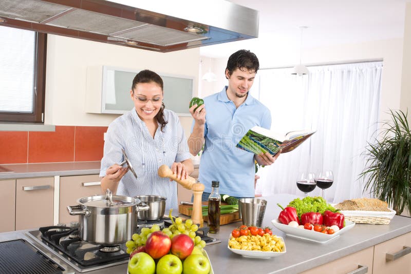 Young happy couple cook in kitchen with cookbook, pasta, vegetable. Young happy couple cook in kitchen with cookbook, pasta, vegetable