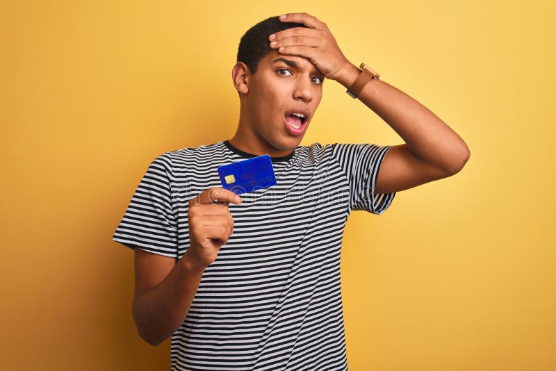 Junge, gut aussehende Araber mit Kreditkarte über isoliertem gelbem Hintergrund gestresst mit Hand am Kopf geschockt lizenzfreie stockfotografie