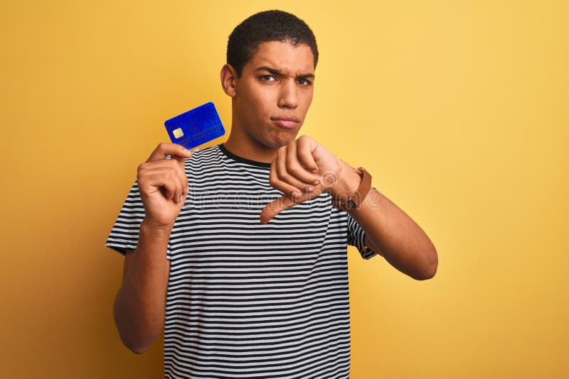 Junge, gut aussehende Araber mit Kreditkarte über isoliertem gelbem Hintergrund mit wütendem Gesicht und negativem Schild, auf dem lizenzfreie stockfotografie