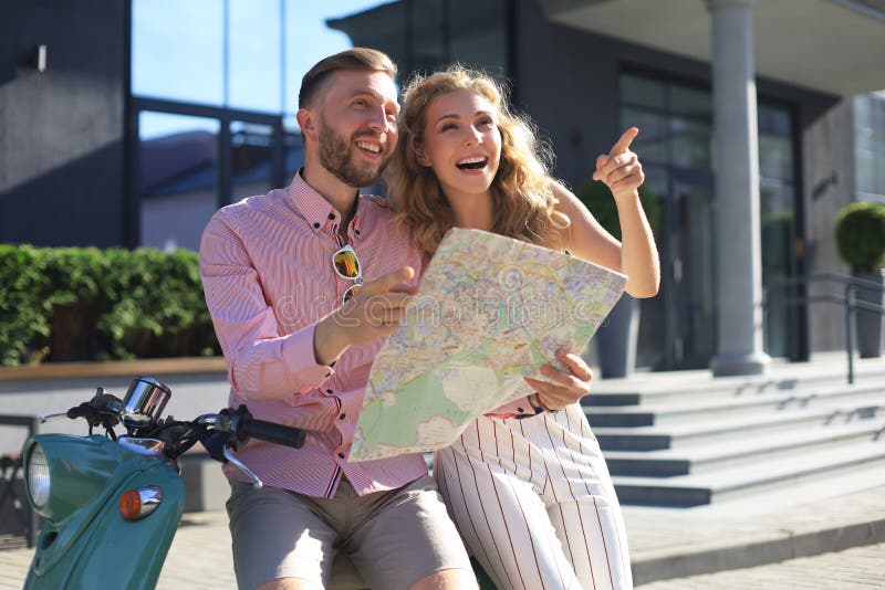 Junge Happy liebevolle Paare, die Karte ansehen und Roller sitzen lizenzfreies stockbild