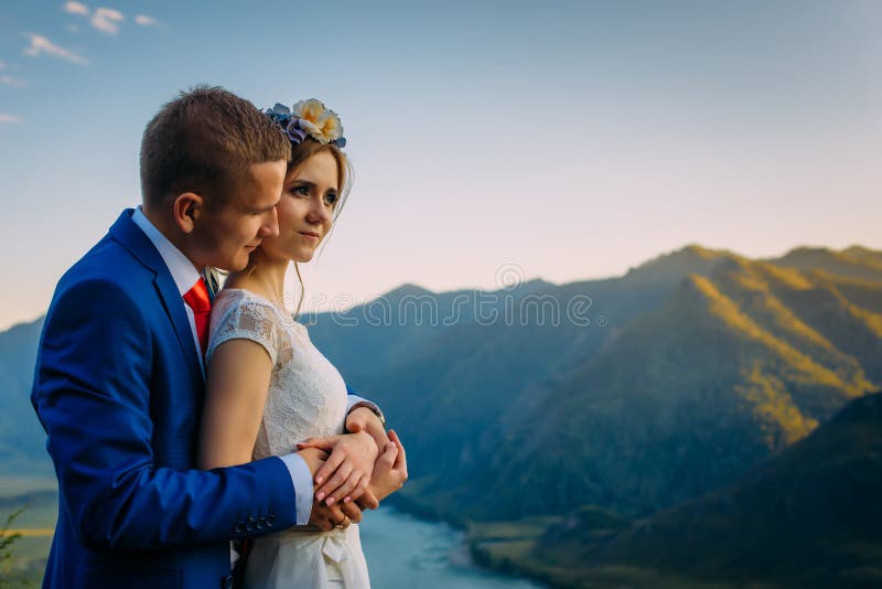 Junge heiraten eben das Paar-, Braut- und Bräutigamküssen und umarmen auf perfekter Ansicht von Bergen, von Fluss und von blaue lizenzfreie stockbilder Junge heiraten eben das Paar-, Braut- und Bräutigamküssen und umarmen auf perfekter Ansicht von Bergen, von Fluss und von blaue lizenzfreie stockbilder