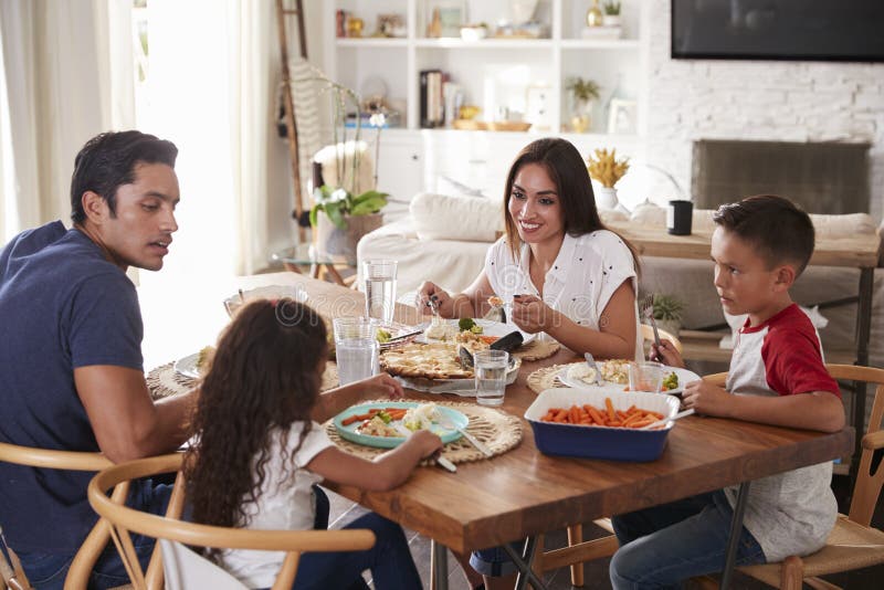 Junge hispanische Familie, die am Speisetische zusammen isst Abendessen sitzt