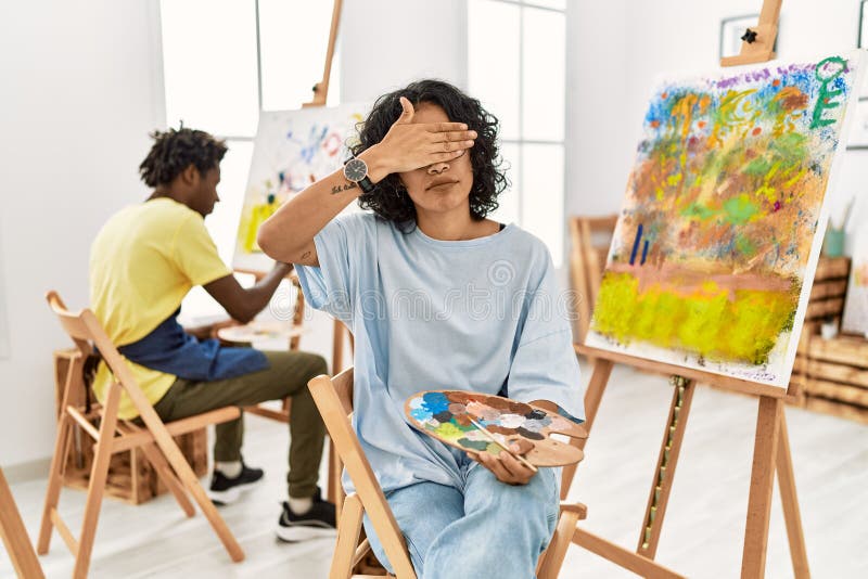 Young hispanic woman at art studio covering eyes with hand, looking serious and sad. sightless, hiding and rejection concept. Young hispanic woman at art studio covering eyes with hand, looking serious and sad. sightless, hiding and rejection concept
