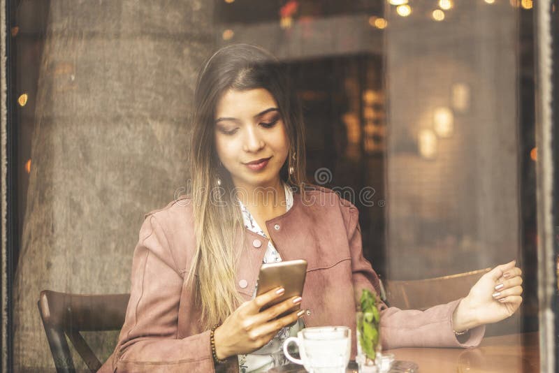 Junge hübsche Frau mit Zelltelefon beim in der Kaffeestube während der Freizeit, attraktives weibliches allein sitzen, das Schaue lizenzfreie stockbilder Junge hübsche Frau mit Zelltelefon beim in der Kaffeestube während der Freizeit, attraktives weibliches allein sitzen, das Schaue lizenzfreie stockbilder