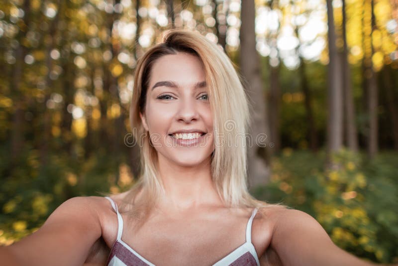 Junge hübsche frohe Frau in einem modischen rosa Kleid macht selfie an einem Telefon im Wald unter den Bäumen an einem sonnigen T stockfoto Junge hübsche frohe Frau in einem modischen rosa Kleid macht selfie an einem Telefon im Wald unter den Bäumen an einem sonnigen T stockfoto