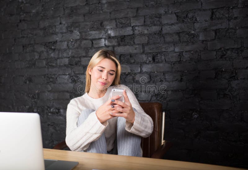 Junge hübsche Studentin-Lesetextnachricht am Handy nach der Arbeit auf Laptop-Computer lizenzfreie stockbilder