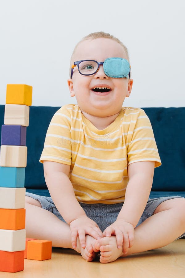 Junge im faulen Augenklappelachen, das im Kinderzimmer und in den Spielen mit Würfeln sitzt stockfoto