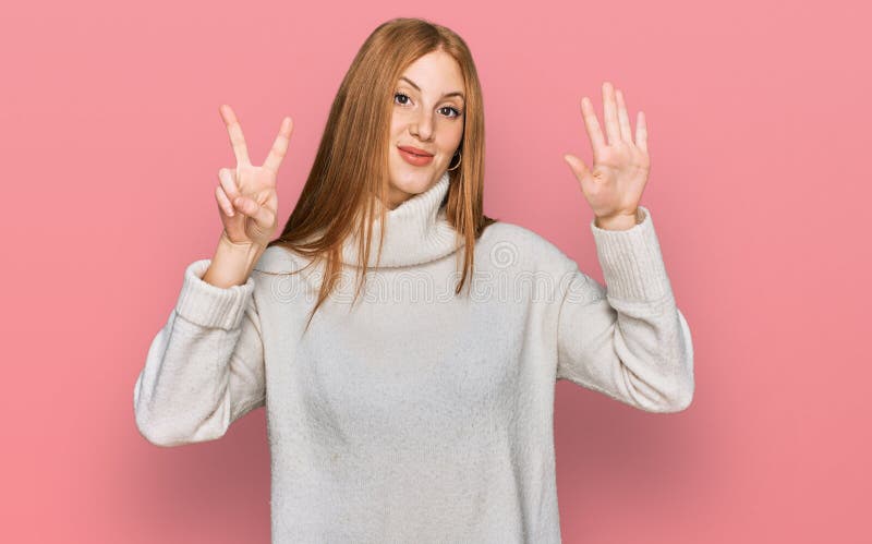 Junge irische Frau, die einen ungezwungenen Winterpullover trägt und mit den Fingern Nummer sieben zeigt und aufzeigt, während sie lizenzfreies stockfoto