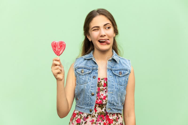 Junge Jugendliche mit blondie langem Haar, Wink an der Kamera, Zunge heraus, hält lolipop und hat lustigen Blick lizenzfreie stockfotografie Junge Jugendliche mit blondie langem Haar, Wink an der Kamera, Zunge heraus, hält lolipop und hat lustigen Blick lizenzfreie stockfotografie
