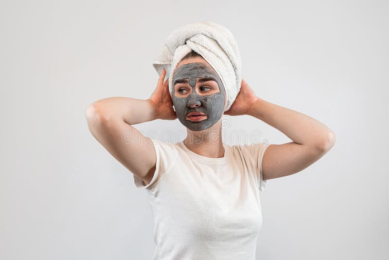 Junge kaukasische Frau im Handtuch auf dem Kopf mit schwarzem Ton oder matter Gesichtsmaske isoliert auf weiß lizenzfreies stockbild