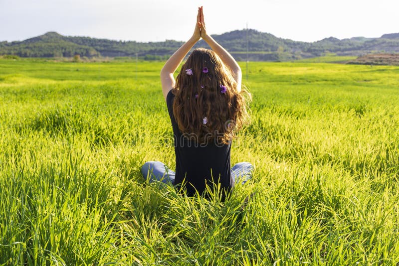 Young caucasian woman red-haired with freckles, resting on a green field at spring sunset, sitting in a yoga position. Meditation, mindfulness, relax. Young caucasian woman red-haired with freckles, resting on a green field at spring sunset, sitting in a yoga position. Meditation, mindfulness, relax