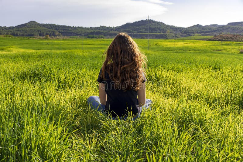 Young caucasian woman red-haired with freckles, resting on a green field at spring sunset, sitting in a yoga position. Meditation, mindfulness, relax. Young caucasian woman red-haired with freckles, resting on a green field at spring sunset, sitting in a yoga position. Meditation, mindfulness, relax