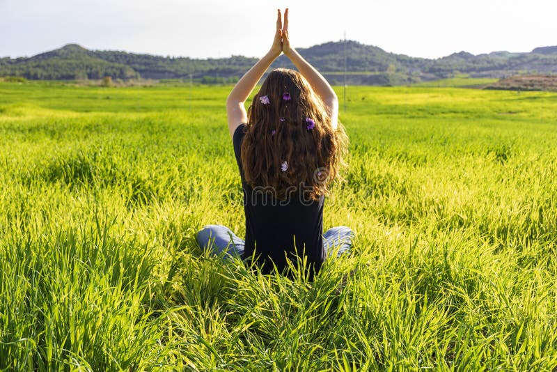 Young caucasian woman red-haired with freckles, resting on a green field at spring sunset, sitting in a yoga position. Meditation, mindfulness, relax. Young caucasian woman red-haired with freckles, resting on a green field at spring sunset, sitting in a yoga position. Meditation, mindfulness, relax